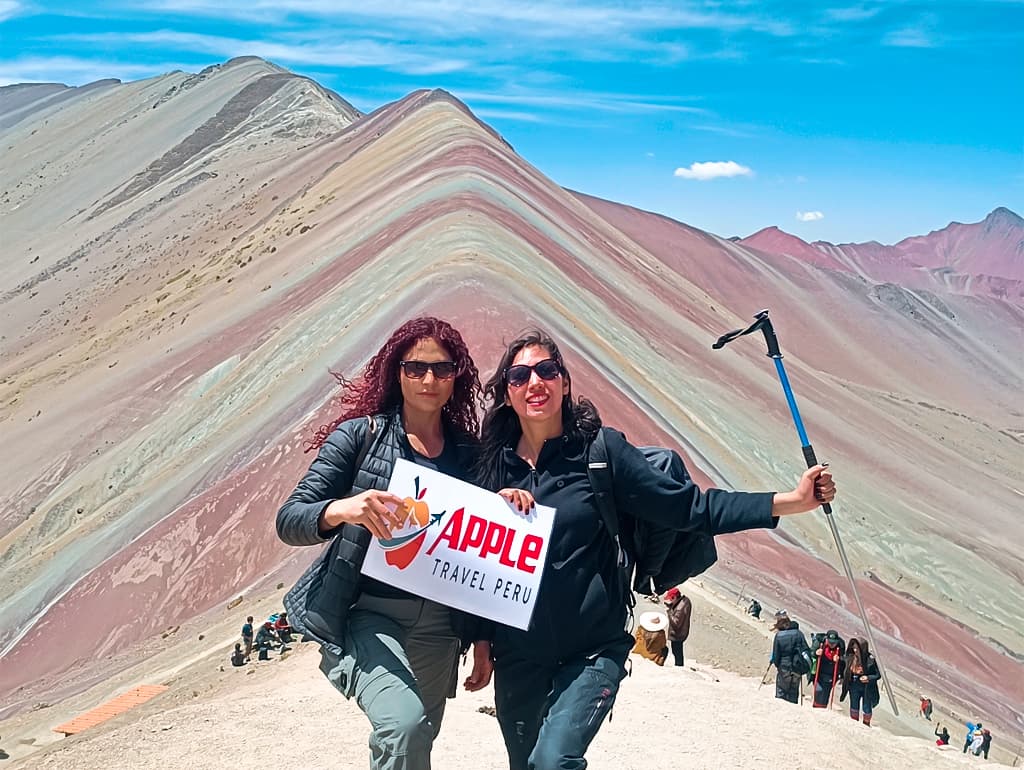 Two female tourists with Apple Travel Peru's placard at Rainbow Mountain Tour